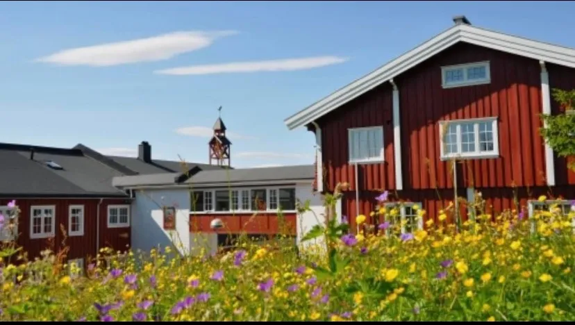 Sommerbilde av hotellet tatt fra oversiden mot villa, overbygd gang og tårnet, blomstereng
