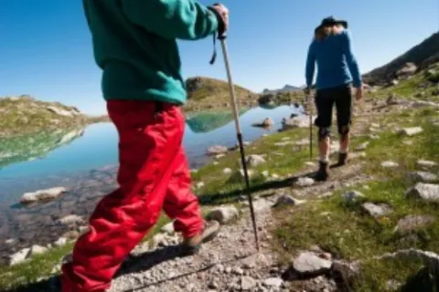 Fottur i fjellet langs blikkstille fjellvatn, skyfri himmel og sommer